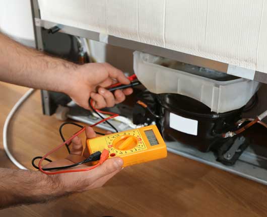 Technician measuring electrical continuity in a freezer circuit using a digital multimeter