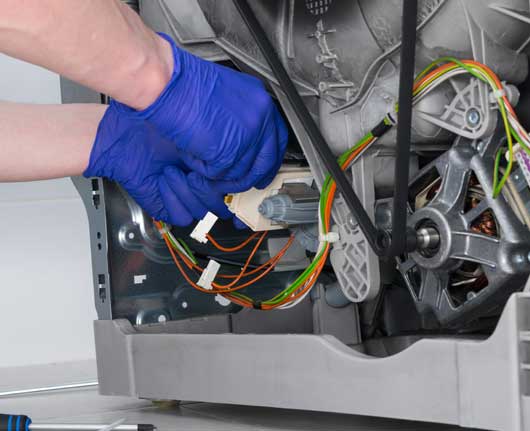 Technician hands repairing internal washer components during emergency washer repair