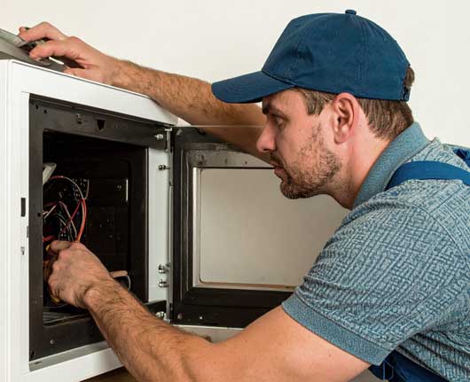 Technician performing microwave repair Orange County on a built-in kitchen microwave